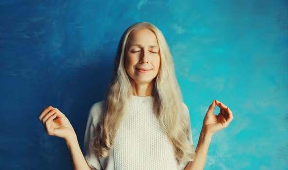 Relaxed caucasian middle aged woman meditates in yoga lotus position with folded arms and closed eyes