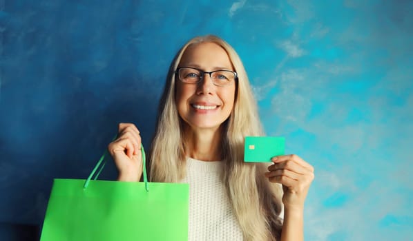 Portrait of happy smiling caucasian middle aged woman holding plastic credit bank card with shopping bags on studio background