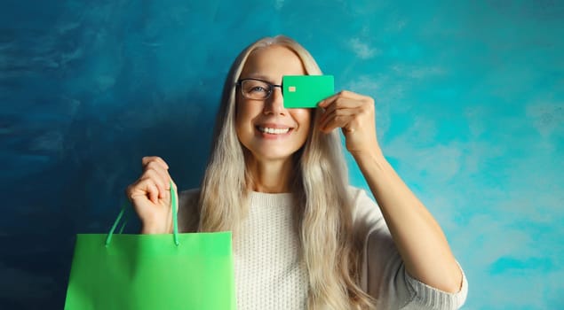Portrait of happy smiling caucasian middle aged woman holding plastic credit bank card with shopping bags on studio background
