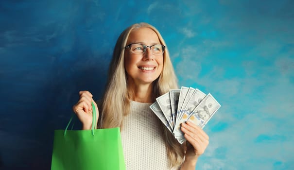 Portrait of happy smiling middle aged woman with shopping bags holding cash money in dollar bills in her hands
