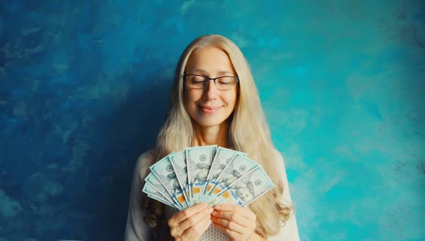 Portrait of happy smiling middle aged woman holding cash money in dollar bills in her hands