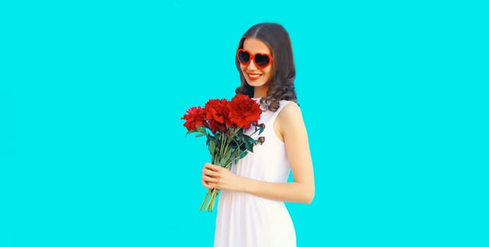 Portrait of beautiful smiling woman with bouquet of red rose flowers in heart shaped sunglasses on blue background