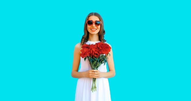 Portrait of beautiful smiling woman with bouquet of red rose flowers in heart shaped sunglasses on blue background