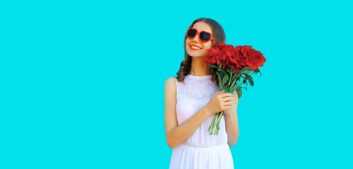 Portrait of beautiful smiling woman with bouquet of red rose flowers in heart shaped sunglasses on blue background