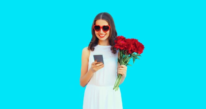 Portrait of beautiful smiling woman with phone and bouquet of red rose flowers in heart shaped sunglasses on blue background