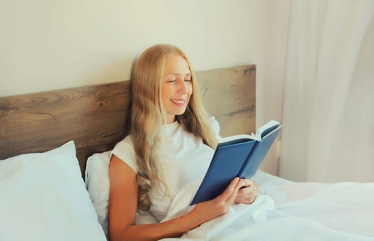 Happy middle aged woman reading book with blank cover while lying on the bed at home