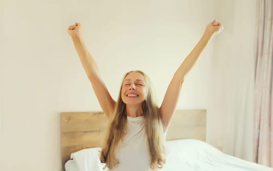 Healthy sleep, relaxed middle aged woman wakes up lying on the bed in bedroom at home