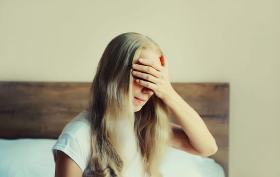 Upset sad crying woman covering her eyes with hands on the bed experiencing mental suffering in bedroom at home