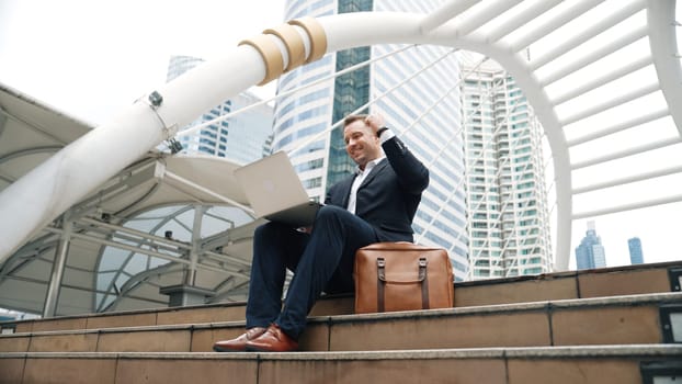 Low angle view of professional business man working on laptop at stairs while celebrate successful project. Caucasian project manager using computer to plan marketing strategy at urban city. Urbane.