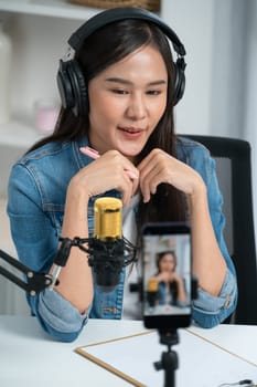 Host channel Asian influencer talking in broadcast wearing headsets on social media live on smartphone recording online, greeting listeners with coaching life or business at modern studio. Stratagem.
