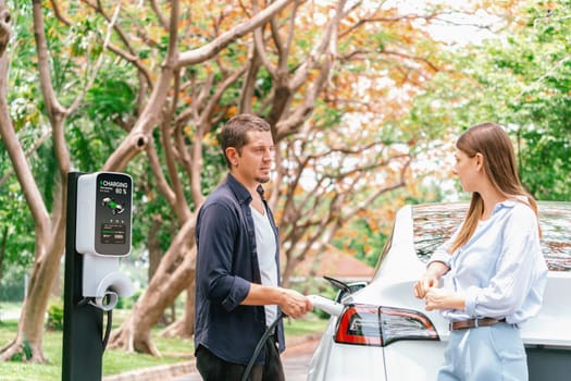 Lovely young couple recharging battery for electric car during autumnal road trip travel EV car in autumnal forest. Eco friendly travel on vacation during autumn. Exalt