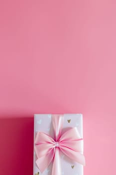 One beautiful gift box with a bow lie from below on a bright pink background with copy space on top, flat lay close-up.