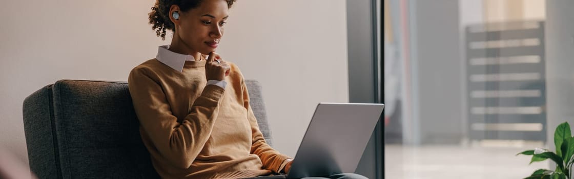 Pretty female freelancer working on laptop while sitting on modern coworking background