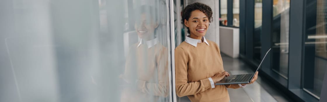 Smiling female entrepreneur using laptop while standing on office background and looks camera