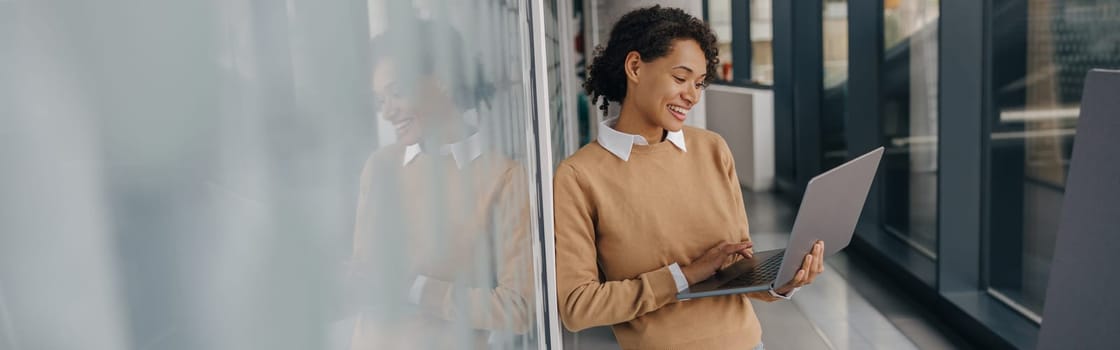 Pretty female freelancer working on laptop while standing on modern coworking background