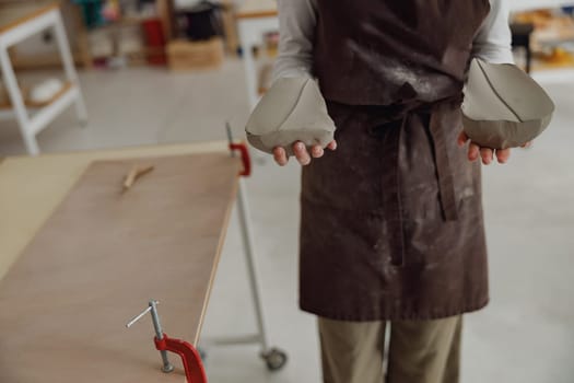 Close up of woman preparing clay to create a mug on a wooden table in pottery studio