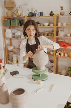 Professional female ceramist work with unfired clay vase in pottery studio. High quality photo