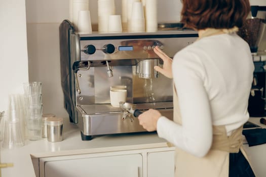 Back view of female barista making coffee in a coffee machine working in cafe. High quality photo