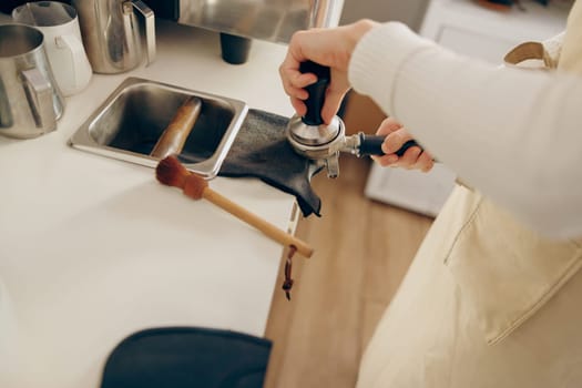 Close-up of barista using a tamper to press ground coffee into a portafilter at the coffee shop