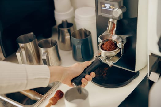 Close up of female barista grinding coffee using professional grinder machine in coffee house