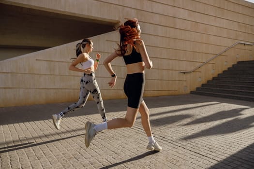 Two young women in sportswear are running on modern buildings background. Active lifestyle concept