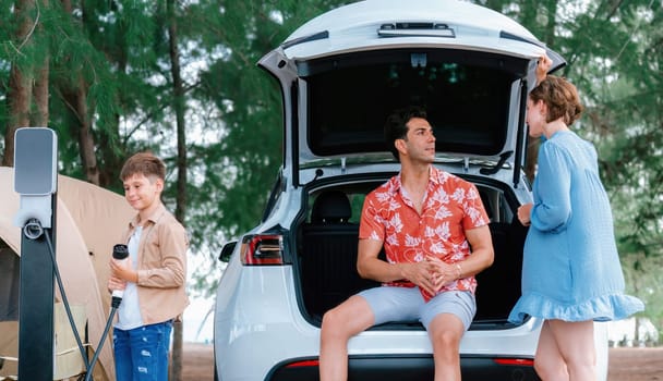 Outdoor adventure and family vacation camping in nature travel by eco friendly car for sustainable future. Lovely family recharge EV car with EV charging station in campsite. Perpetual