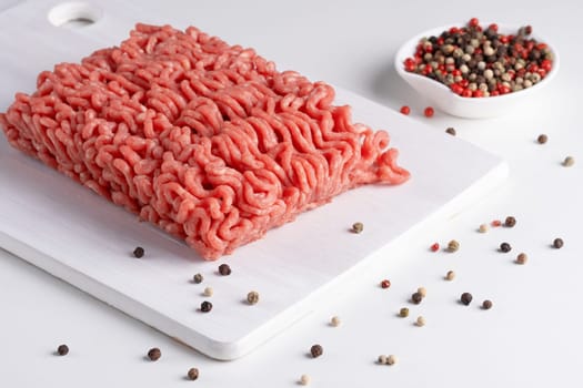 Fresh raw minced meat and peppers on a white table, close-up.