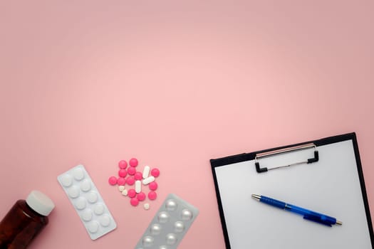 Flat lay of a bottle of medicine, medication blister packs, pills, clipboard and pen on a pink background for the concept of medical note taking and healthcare