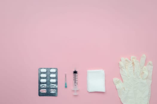 Flat lay of medication blister packs, syringes, gauze, and latex gloves on a pink background for the concept of medical and healthcare