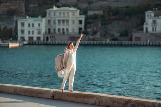 Happy blonde woman in a white suit and hat posing at the camera against the backdrop of the sea.