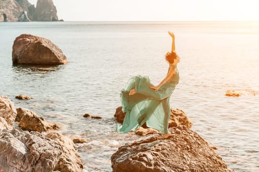 Woman green dress sea. Woman in a long mint dress posing on a beach with rocks on sunny day. Girl on the nature on blue sky background