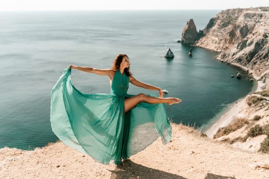 Woman green dress sea. Female dancer posing on a rocky outcrop high above the sea. Girl on the nature on blue sky background. Fashion photo