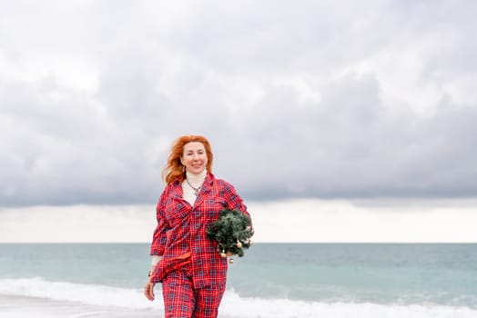 Sea Lady in plaid shirt with a christmas tree in her hands enjoys beach. Coastal area. Christmas, New Year holidays concep.