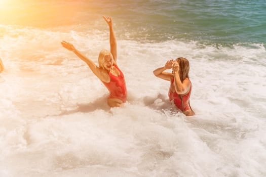 Women ocean play. Seaside, beach daytime, enjoying beach fun. Two women in red swimsuits enjoying themselves in the ocean waves and raising their hands up