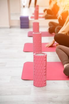 A group of six athletic women doing pilates or yoga on pink mats in front of a window in a beige loft studio interior. Teamwork, good mood and healthy lifestyle concept