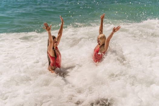 Women ocean play. Seaside, beach daytime, enjoying beach fun. Two women in red swimsuits enjoying themselves in the ocean waves and raising their hands up