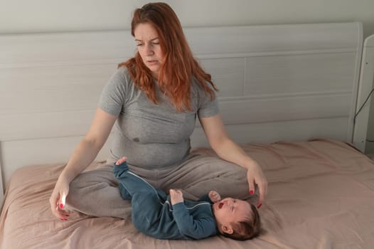 A Caucasian woman sits on a bed next to a crying baby. Postpartum depression