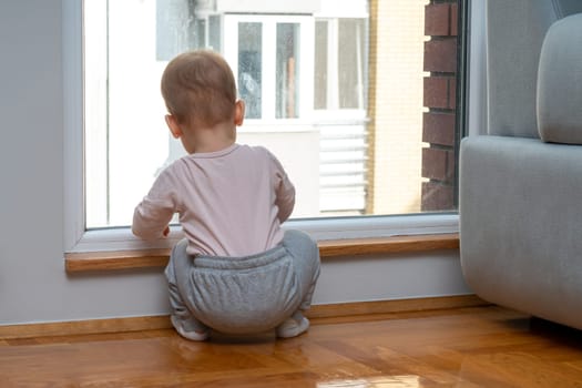 Sitting quietly by the window, a baby scans the outside, eagerly awaiting the moment their dad walks back home from work. Concept of hope and waiting