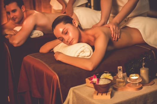 Caucasian couple customer enjoying relaxing anti-stress spa massage and pampering with beauty skin recreation leisure in warm candle lighting ambient salon spa at luxury resort or hotel. Quiescent