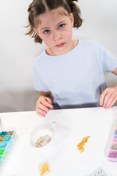 Little girl enjoys crafting colorful bracelets with vibrant clay beads set.