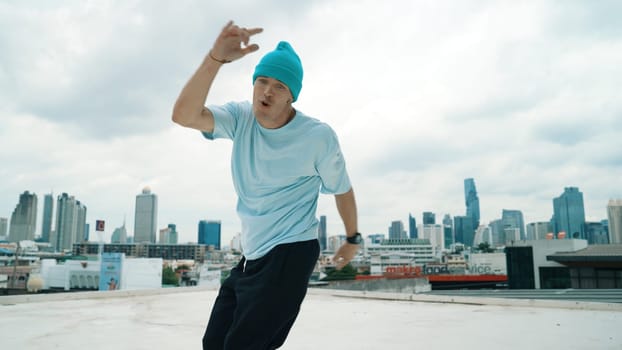 Caucasian B-boy dancer practicing street dancing at rooftop with city urban view. Motion shot of young man performing street dance by moving with hip -hop music. Outdoor sport 2024. Endeavor.