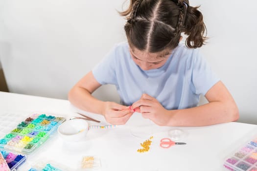 Little girl enjoys crafting colorful bracelets with vibrant clay beads set.