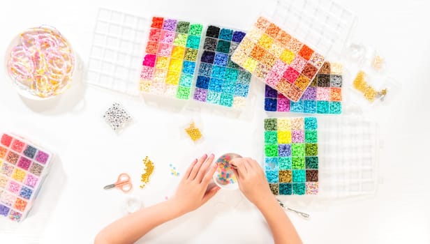 Flat lay. Little girl enjoys crafting colorful bracelets with vibrant clay beads set.