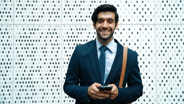 Portrait image of successful young business man looking at camera while hold phone with white background. Attractive caucasian investor or project manager standing at building. Close up. Exultant.