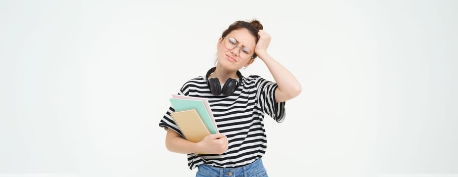 Image of upset young woman, student in glasses complains at difficult task at university, holding notebooks, forgot to do something, white background.