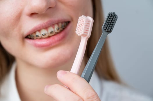 Cropped portrait of young smiling woman with braces holding two toothbrushes