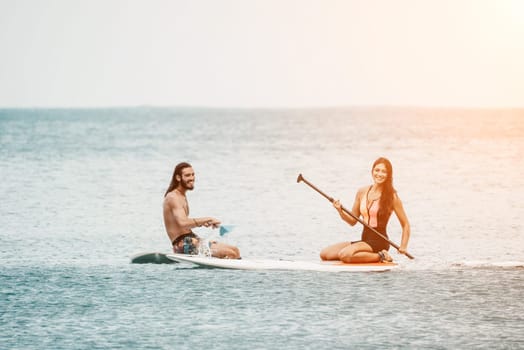 Sea woman and man on sup. Silhouette of happy young woman and man, surfing on SUP board, confident paddling through water surface. Idyllic sunset. Active lifestyle at sea or river