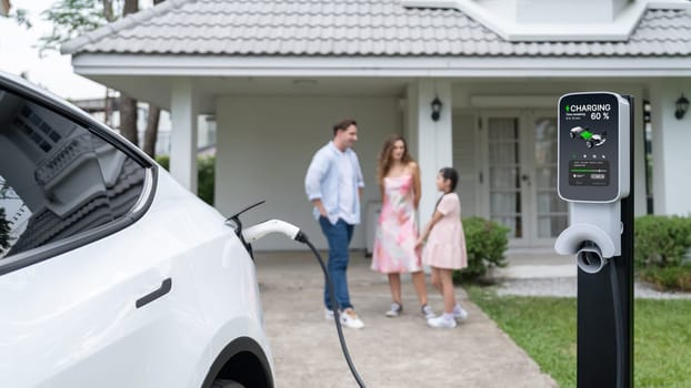 Focused electric vehicle recharging battery from home charging station for EV car powered by alternative and sustainable energy for modern environmental family on blur background. Panorama Synchronos