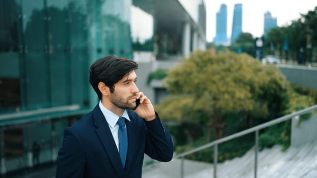 Skilled caucasian project manager calling phone while walking at city with blurred background. Skilled businessman using smart phone talking to project manager with blurred background. Exultant.