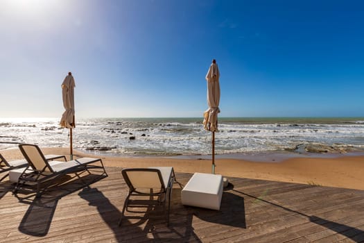 Chaise lounges and umbrellas near the sand on the coast of the azure sea and against the blue sky,